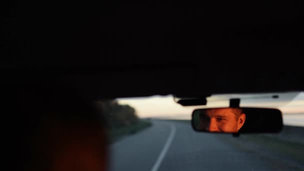 Unge man i bilen. Glad positiv kaukasisk man kör bil snabbt och titta på backspegeln med leende. suddig bakgrund. — Stockvideo