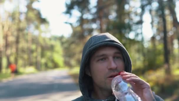 Um homem na floresta ou no parque bebe água de uma garrafa de lixo de plástico depois de um duro exercício de jogging — Vídeo de Stock