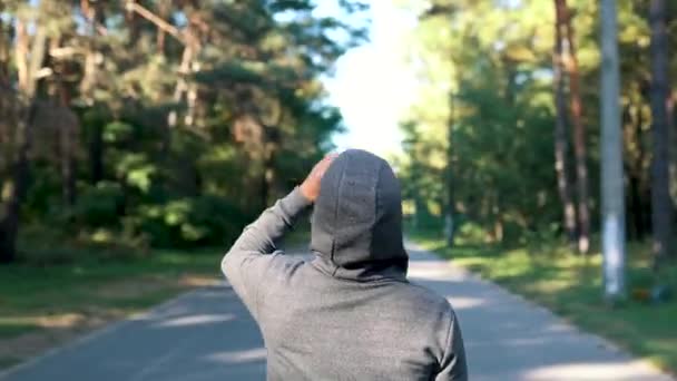 Um homem na floresta ou no parque bebe água de uma garrafa de plástico após um duro exercício de jogging. Câmera movimento circular — Vídeo de Stock