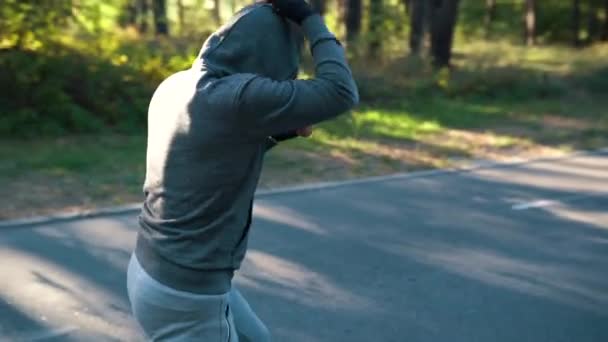 Egy férfi a parkban egy árnyékban bokszol, kötéssel a kezén. Lassú mozgás koncepció. A kamera körkörös mozgása — Stock videók
