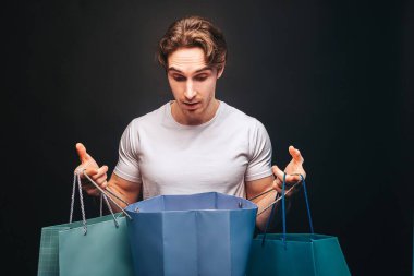 Açılmış alışveriş çantasına bakan şaşırmış adam.