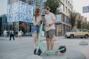 Genç ve çekici çift elektro scooter kullanmaya çalışıyor.