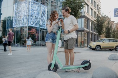 Genç ve çekici çift elektro scooter kullanmaya çalışıyor.