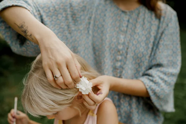 Madre joven está fijando el pelo de su hijo en el jardín. Tiempo en familia. — Foto de Stock