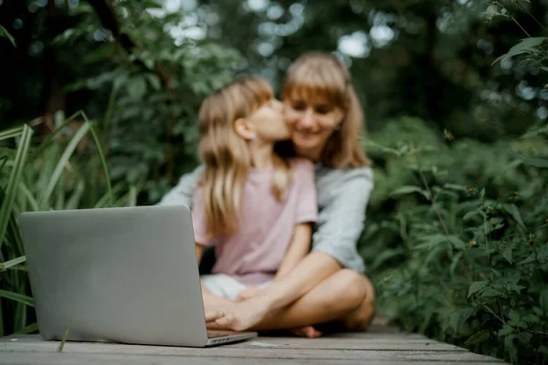 Дитина цілує свою маму, граючи на ноутбуці в саду — стокове фото
