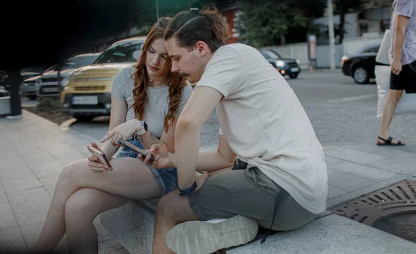 Очаровательная девушка и привлекательный парень используют свои телефоны в городе Стоковое Фото