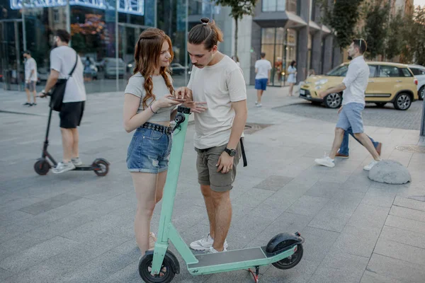 Mujer atractiva joven está enseñando a su novio cómo utilizar scooter eléctrico Fotos De Stock Sin Royalties Gratis