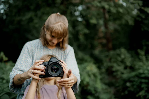La madre sta insegnando alla sua giovane figlia ad usare una macchina fotografica all'esterno nella natura primaverile Foto Stock Royalty Free