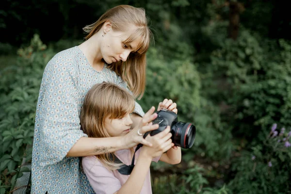 Madre está enseñando a su hija pequeña a usar una cámara afuera en la naturaleza de primavera Imagen De Stock