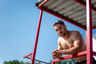 Sahilde formda bir vücut geliştirici. Kumsaldaki çekici genç adam cankurtaranı..