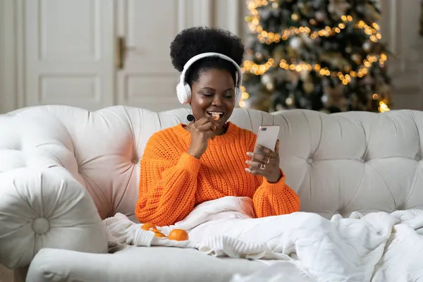 Matin de Noël à la maison : repos de la fille noire après la fête de nouvel an dans le lit défiler les photos dans les médias sociaux — Photo