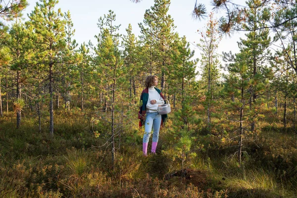 Случайные девушки в резиновых сапогах наслаждаются теплым солнечным днем ходить собирать клюкву в осеннем лесу. Осенний сезон — стоковое фото