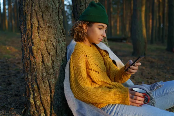 Cestovatel žena textování nebo čtení nebo e-mail v smartphonu posezení uvolněný s šálkem čaje pod stromem — Stock fotografie