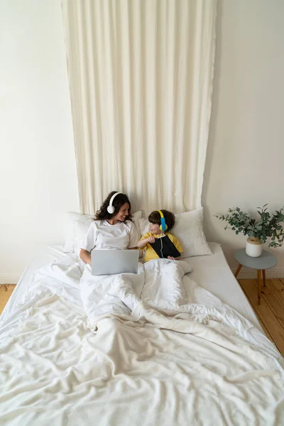 Anya és fia együtt dolgoznak és tanulnak az ágyban laptoppal és digitális tablettel a hálószobában — Stock Fotó