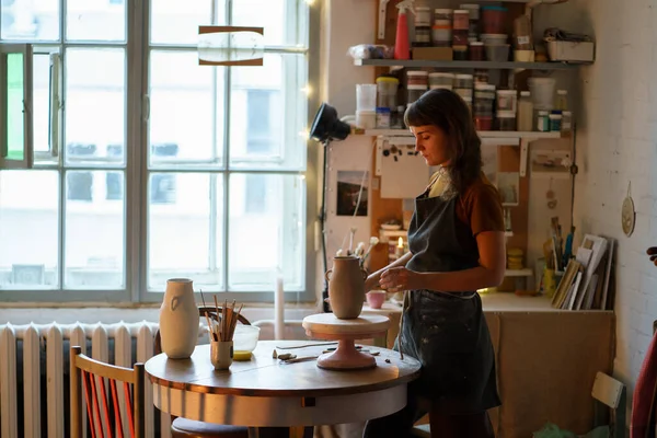 Stüdyodaki seramist kız: Önlüklü genç serbest çalışan kadın mutfak malzemeleri dükkanı için çömlek yapıyor. — Stok fotoğraf