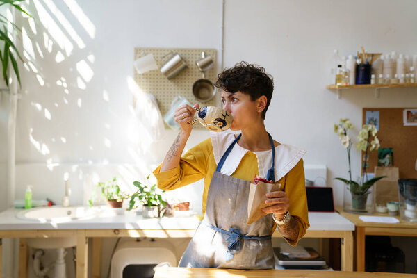 Female ceramist drink coffee and eat snack in art studio at break from master class produce pottery