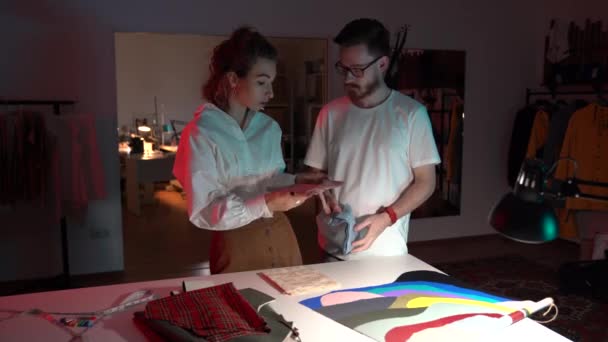 Un par de diseñadores miran a través de muestras textiles. Sastre autónomo y costurera en taller — Vídeo de stock