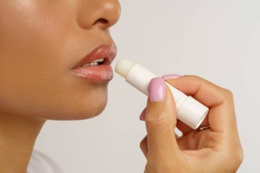 African woman apply hygienic balsam lipstick for lips moisturizing and protection from cold and wind clipart