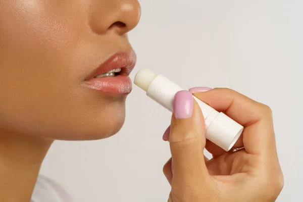 Wanita Afrika menerapkan lipstik balsam higienis untuk pelembab bibir dan perlindungan dari dingin dan angin — Stok Foto