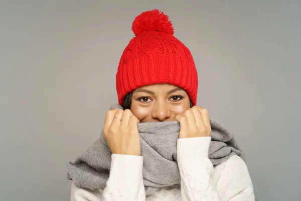 Vtipná mladá africká žena ve svetru, pletená vlněná čepice skrývající úsměv pod teplým šátkem zakrývajícím tvář — Stock fotografie