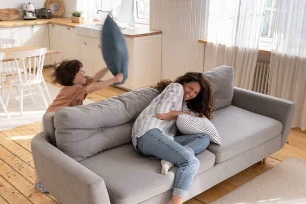 Fröhliche Mutter mit Vorschulkind kämpft gegen Kissen im Wohnzimmer. Lustige Familienaktivitäten zu Hause auf — Stockfoto