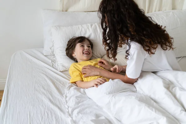 Feliz madre haciendo cosquillas pequeño hijo riendo en la cama después de despertar en la mañana del fin de semana. Amor y familia —  Fotos de Stock