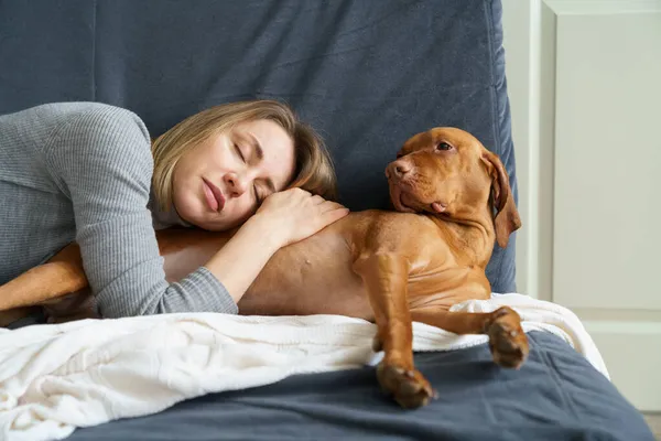 Mulher cansada dormir com cão tomando animal de estimação da clínica veterinária para recuperação da cirurgia em casa — Fotografia de Stock