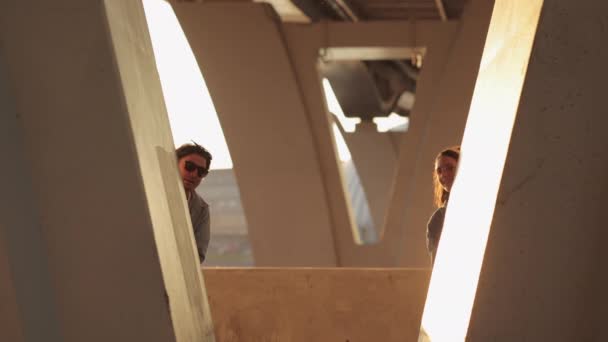 Juguetona pareja joven posando en el espacio urbano escondido mirando desde el puente agitando las manos feliz sonrisa — Vídeos de Stock