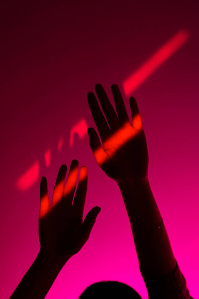 Woman arm gesturing with open hand over fashion pink background, neon red spot on wrist. Minimalism.