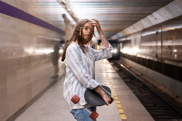 Chica casual joven en la plataforma esperando llegada del tren. Mujer patinadora en la estación de metro subterráneo — Foto de Stock