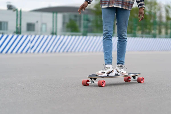 Kobieta na longboard: przycięty obraz czarnej kobiety nosić modne trampki buty i dżinsy na deskorolce — Zdjęcie stockowe