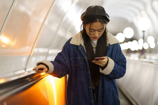 Kız akıllı telefonsuz yaşayamaz. Sosyal medyadan bağımlı Koreli kadın yürüyen merdivende telefonu tutuyor. — Stok fotoğraf