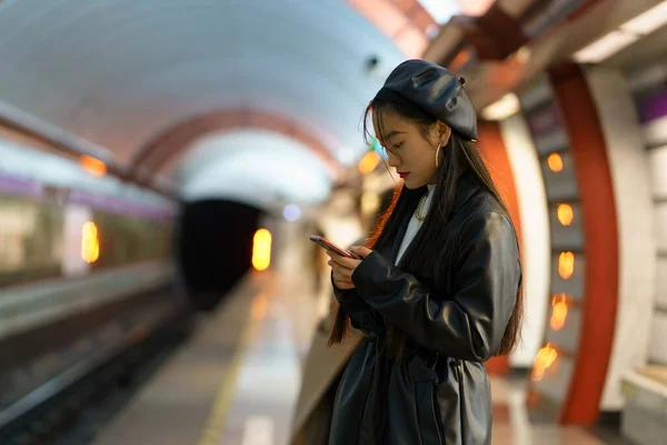 Metro istasyonunda akıllı telefonu olan Çinli bir kız. Tarz sahibi kadın sosyal medyada treni bekliyor. — Stok fotoğraf