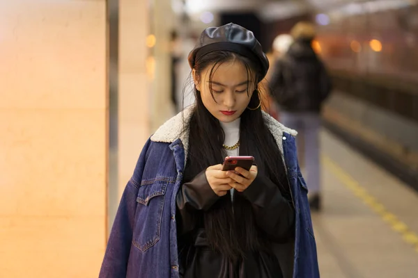 Korejská mladá žena SMS on-line na stanici metra držet smartphone, číst sms nebo rezervovat vstupenky — Stock fotografie