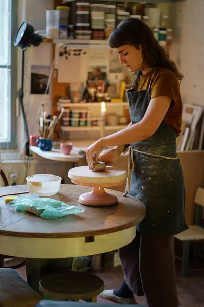 Ung kvinnlig krukmakare arbetar med lera på keramik hjul i kreativa utrymme eller professionell studio — Stockfoto
