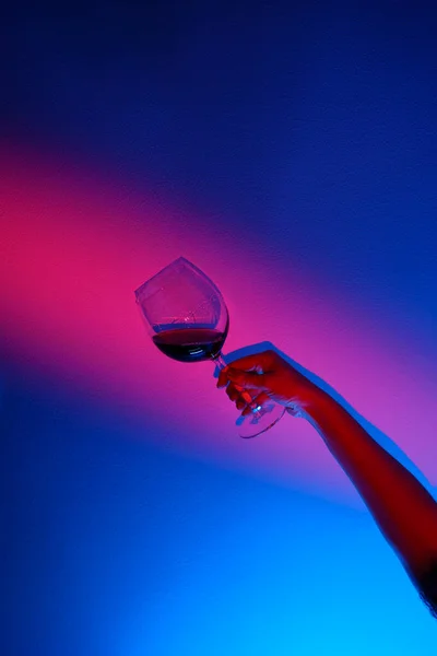 Detailní záběr ženské ruky držící sklenici vína přes modrou stěnu, neonově modrý pruh na stěně. — Stock fotografie
