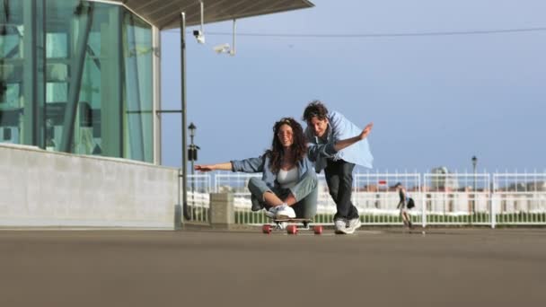Cuplu să se distreze pe longboard: de sex masculin împinge înapoi de femeie veselă stând pe skateboard și râzând — Videoclip de stoc