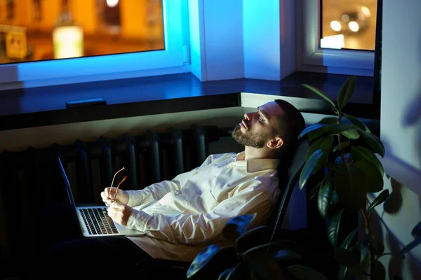 Yorgun genç işadamı ya da programcı karanlık ofiste gözleri kapalı oturur ve fazla mesai yapar. — Stok fotoğraf