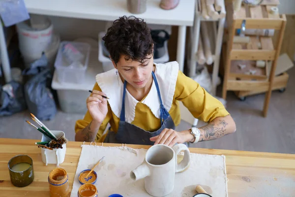 Woman artisian in pottery studio drawing on clay handmade teapot, female ceramist at work — Stock Photo, Image