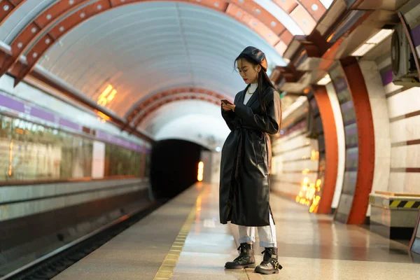 Chica asiática de moda esperar tren en la plataforma del metro comprobar correo electrónico o horario en línea en el teléfono inteligente — Foto de Stock