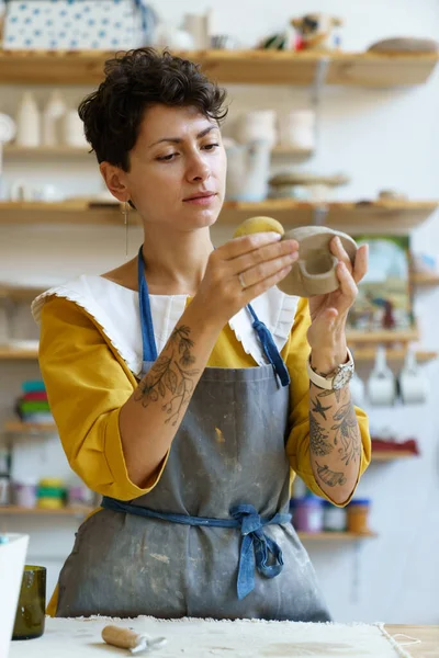 Натхненна жінка використовує губку для поглинання води на глиняному посуді, відвідуючи керамічну майстерню — стокове фото