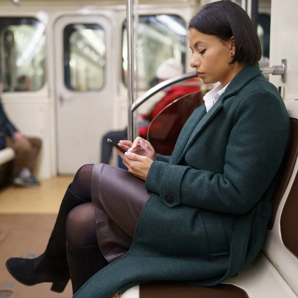 Tükenmiş afro-amerikan kadın ofis çalışanı metro treninde akıllı telefonla işten eve dönüyor. — Stok fotoğraf