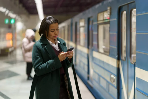 Sosyal medya bağımlılığı. Metro istasyonundaki Afrikalı kadın metro istasyonunda interneti tarıyor. — Stok fotoğraf
