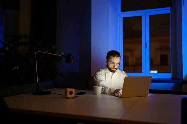 Mladý podnikatel workoholik zůstat pozdě v temné kanceláři práce na spuštění nápadu nebo strategie na notebooku — Stock fotografie