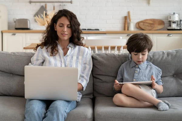 Fiatal üzletasszony anya dolgozik otthonról kisgyerek fia játszani tabletta ülni kanapén a nappaliban — Stock Fotó