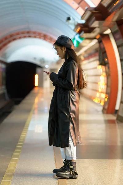 Chica asiática de moda esperar tren en la plataforma del metro comprobar correo electrónico o horario en línea en el teléfono inteligente — Foto de Stock