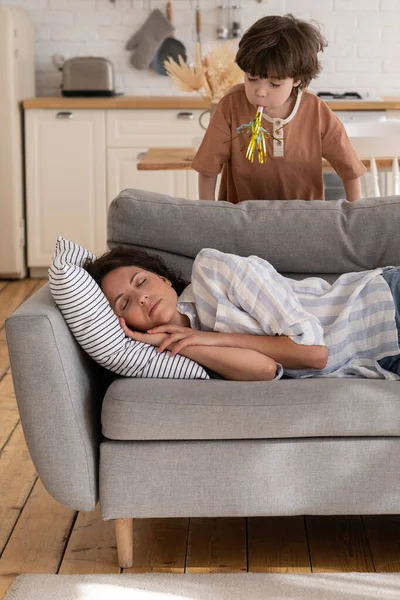 Maman fatiguée dort sur le canapé ne prête pas attention aux enfants bruyants. Mère célibataire se détendre avec enfant faire du bruit — Photo