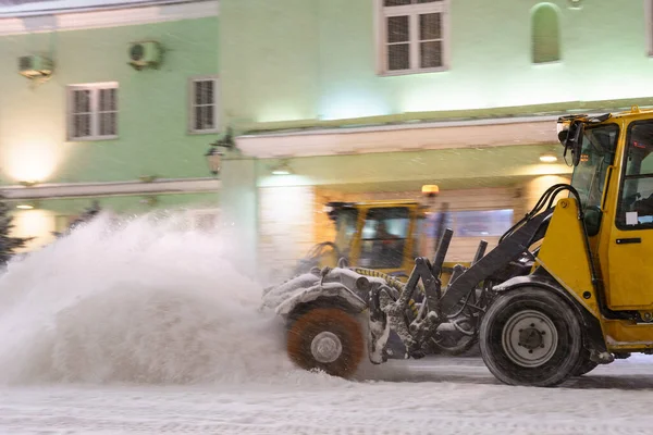 Śnieg pług ciągnika czystej ulicy w nocy w burzy. Samochód do usuwania śniegu na drodze miejskiej po opadach śniegu — Zdjęcie stockowe