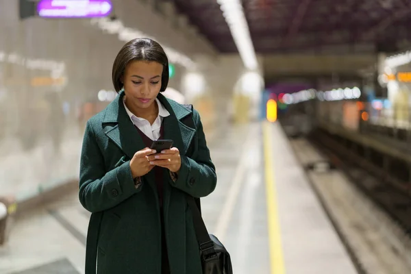 Ciddi iş kadını cep telefonundaki iş e-postasına odaklanmış yeraltında tren bekliyor. — Stok fotoğraf