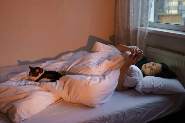 Θλιβερή γυναίκα με smartphone στο κρεβάτι με γάτα, αίσθημα έλλειψης ενδιαφέροντος και κινήτρου στη ζωή — Φωτογραφία Αρχείου